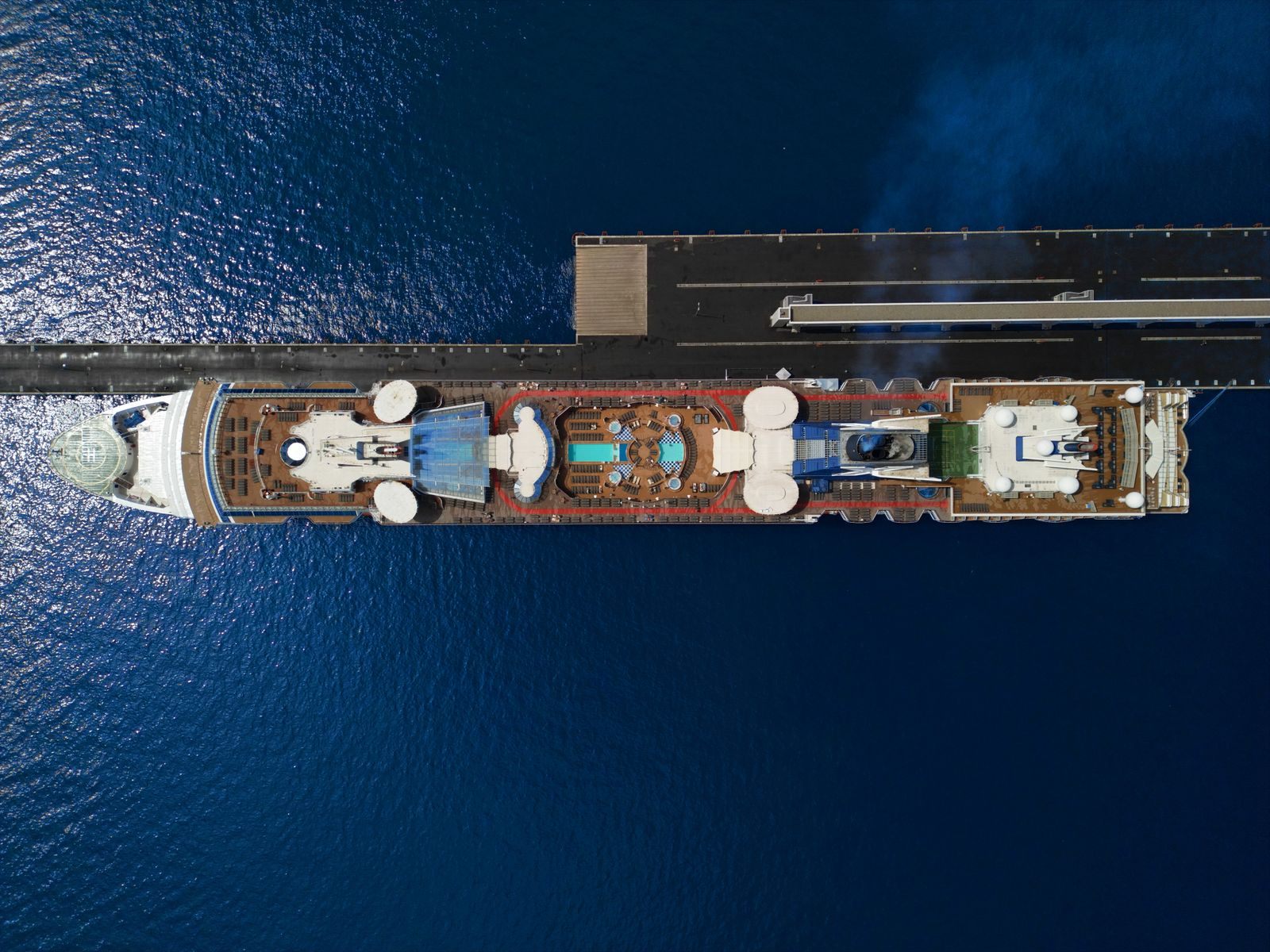 Aerial view of a cruise ship moored at a pier, its pool deck and sun loungers below, the trip where knowing how to save money on a cruise pays off