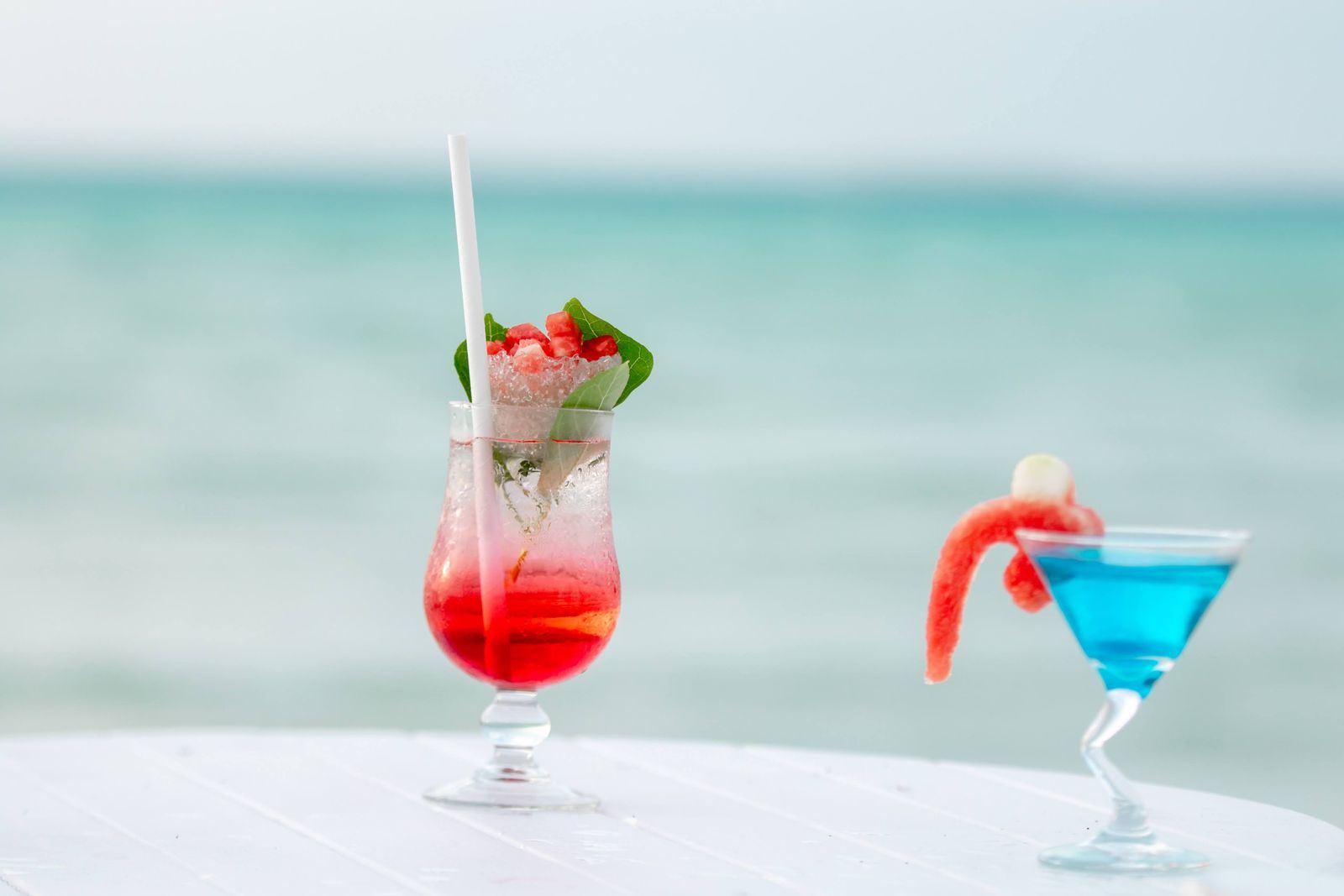 Two colorful cocktails on a table above a turquoise sea