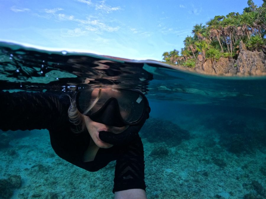 Snorkeler in a mask swimming at the surface near a rocky tropical shore