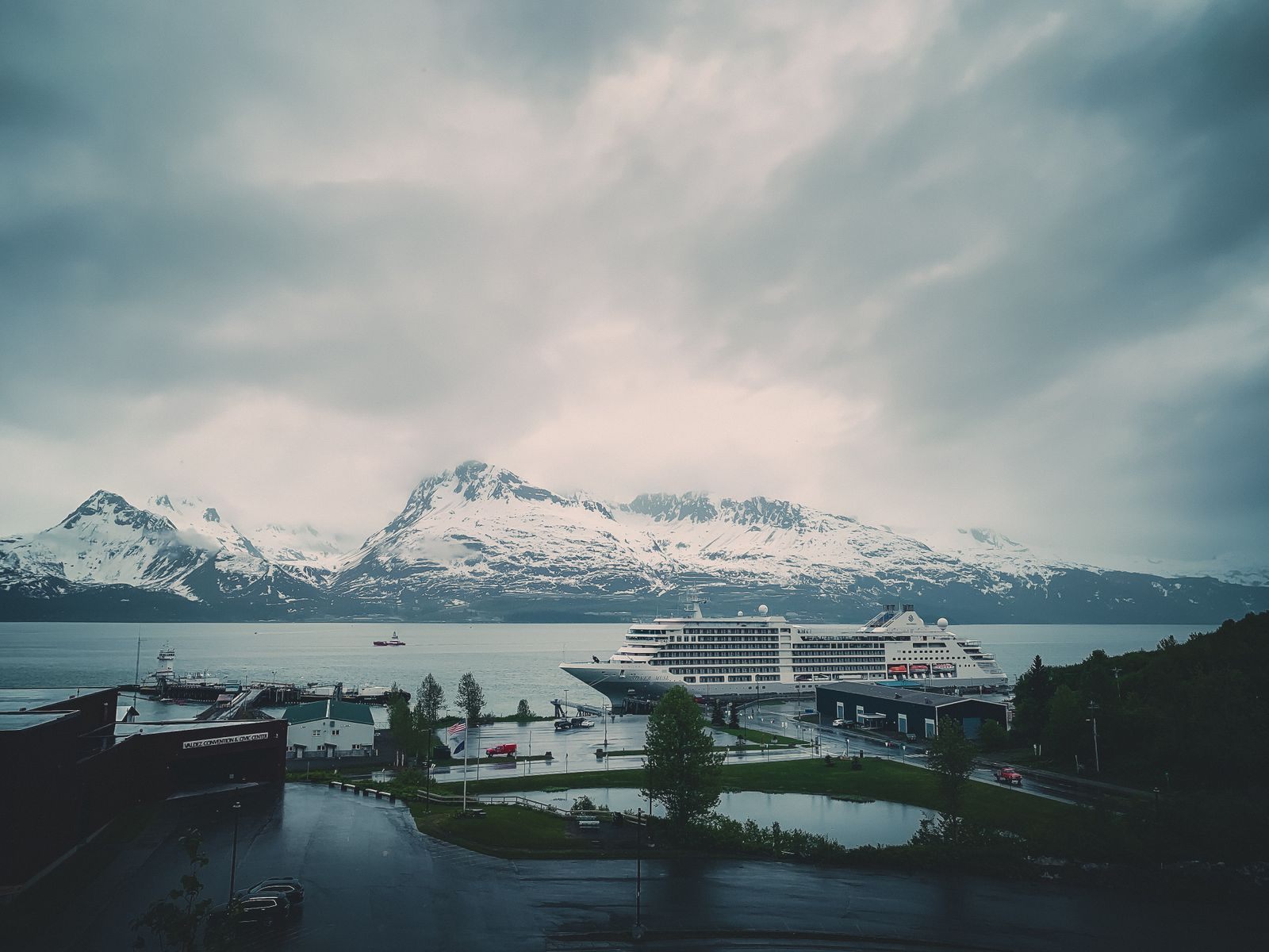 Cruise ship docked at a pier beneath snow-capped mountains