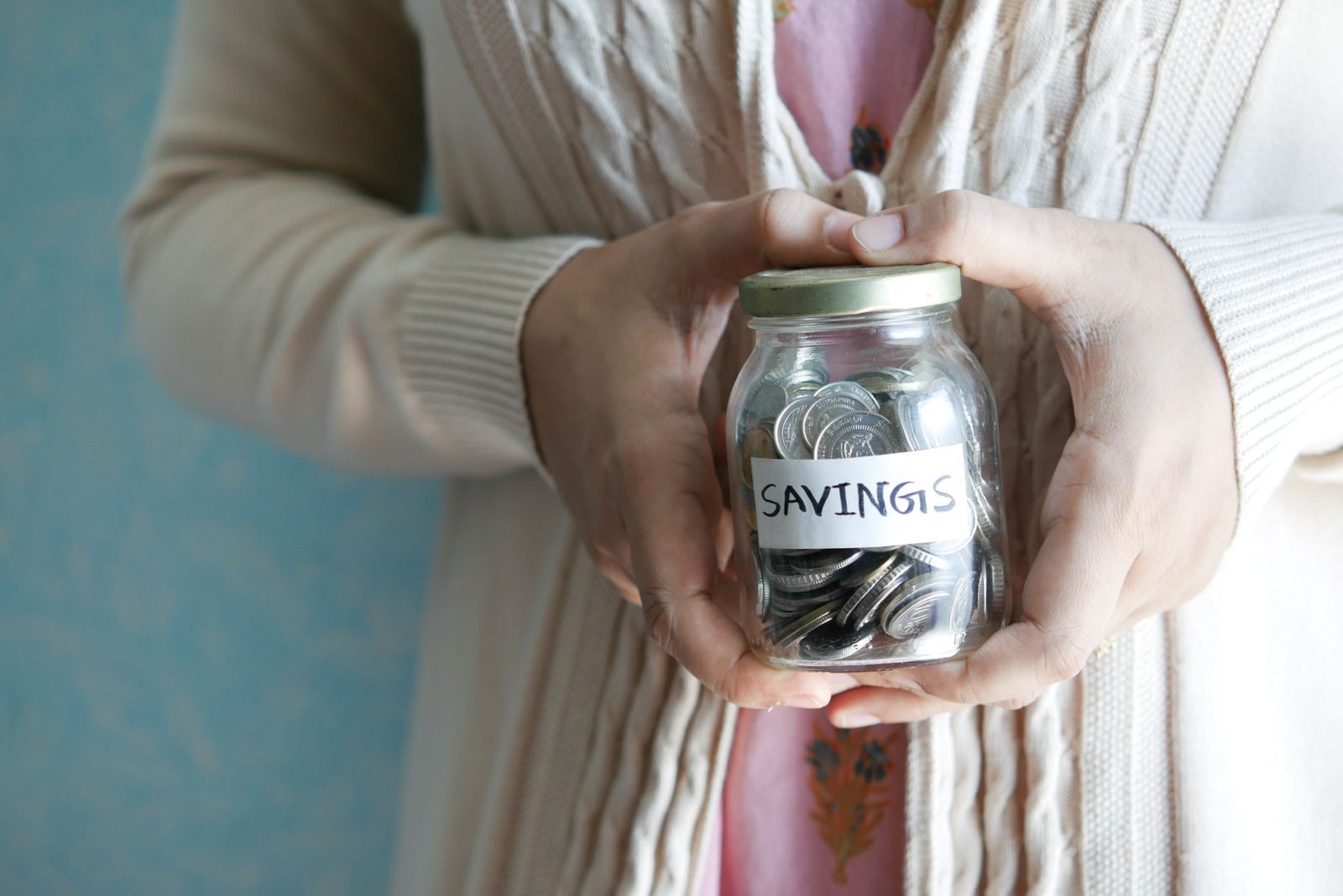 Glass savings jar of coins held in two hands, the start of saving for a cruise