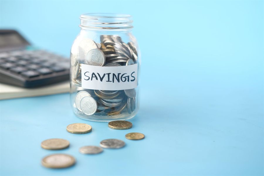 Glass jar labeled savings filled with coins beside a calculator